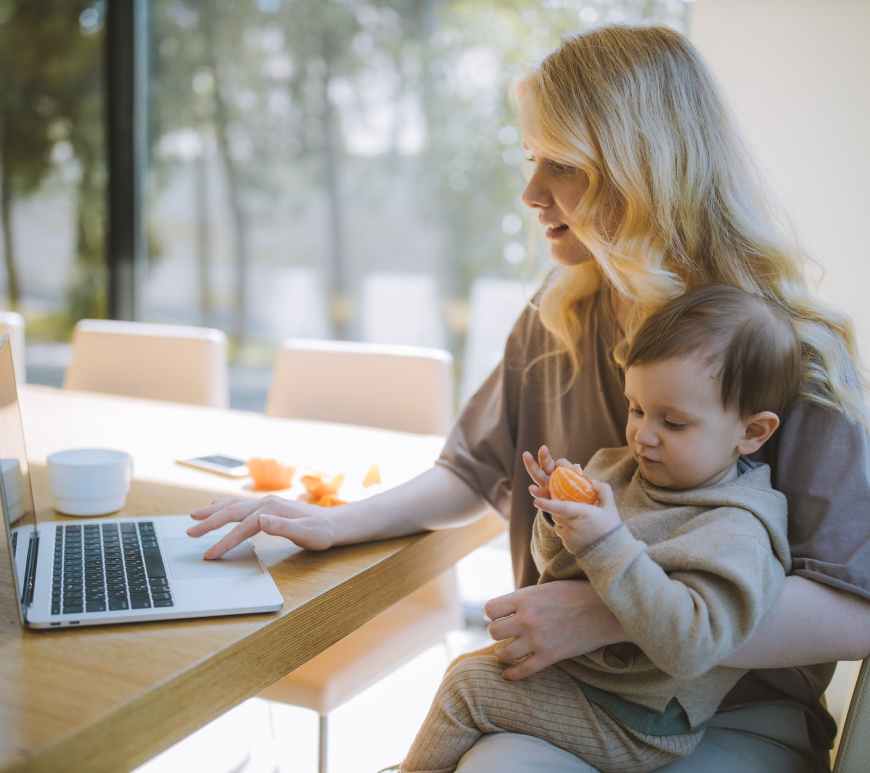 madre con bebé trabajando frente a laptop
